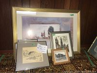 Eight framed art pieces staged on carpeted floor, featuring a large print at back and smaller architectural sketches and prints in front, including a labeled Roy Thompson Hall sketch.