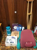 Photo shows Life Source digital blood pressure machine with wrist cuff alongside medical and wellness aids including wooden crutches, OBUS FORME back rest, insulated jug, foot massager, and boxed items.