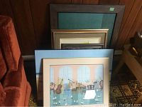 Overview showing five framed prints stacked against a wood-paneled wall on a carpeted floor, including the L. Sanderson print in front.