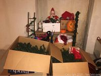 Boxes with disassembled artificial green Christmas trees and red and white knitted stockings inside. Top shelf shows vintage Santa Claus figure and Halloween pumpkin light.