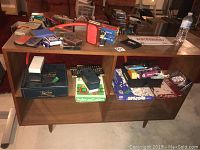 Shelf with various games, including Snakes and Ladders and Monopoly, boxed and loose cards, small boxed games, and others.