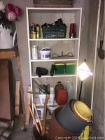 Full view of white bookshelf loaded with garden and yard supplies including gas can, pots, tools, and planter with faux flowers