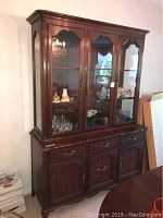 Front view of two-piece mahogany cabinet with upper glass display filled with glassware and lower buffet with drawers and doors.