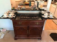 Wood buffet cabinet with expandable side wings open, slate style top, drawer and cabinet doors with brass hardware, wood carved details.