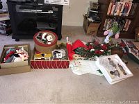 Full view of assorted Christmas decorations including boxes, stockings, wreath, doily, and figurines arranged on the floor in front of a TV stand.