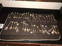 Full display of approximately 50 souvenir spoons arranged on dark felt with various designs and crests.
