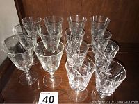 Front view of fourteen assorted crystal wine glasses in two rows on wooden surface, showing varying designs and shapes.