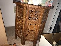Front angle view of the carved wood octagonal table showing detailed floral carving on the side panels and top edge.