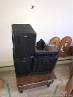 Sony audio system with two speakers and a stack with other electronics placed on a wooden table against a white wall.