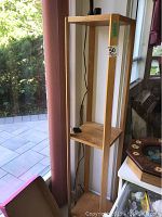 Wooden 3-shelf stand placed near window with attached black adjustable desk lamp.