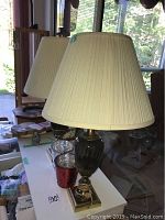Photo of two vintage lamps with pleated fabric shades on a table near window.