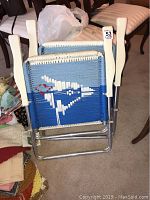 Two folded Artisan Blue Jay folding lawn chairs, showing the blue and white corded backs with Blue Jay bird design, folded compactly.