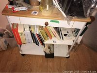 Front view of kitchen trolley showing wood top, white single drawer with wooden knob, and shelves holding books and other items.