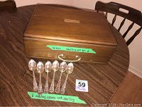 Closed wooden flatware casket on table with six silver plate teaspoons displayed in front.