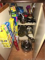 Shelf with boxed pasta machine, rolls of food wrap, saucepans, metal utensils arranged