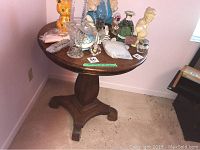 Photo of antique round wood table showing the full pedestal base with curved claw feet and the round top surface with assorted items on it.