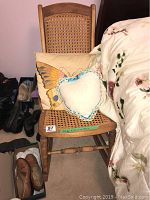 Front view of antique nursing rocker with cane seat and backrest, showing the two decorative pillows: butterfly and heart-shaped lace pillow.