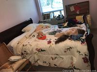 Photo showing queen size bed with dark brown wooden sleigh-style headboard and white floral bedding with various pillows and items on bed