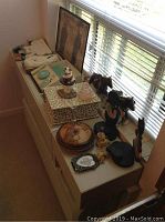 Wide view showing all items on top of dresser, including framed print, draft horse statues, white rabbit fur slippers, cat-themed decor, dresser jar, small metal picture frame, and boxed dresser set with tray, comb, brush.