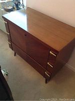 Front side of a polished cedar chest with two drawers and brass trapezoidal handles and corner accents, standing on short legs.