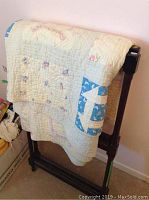 Antique quilt displayed on wooden folding blanket rack from front.