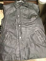 Front view of black leather coat with snap buttons, collar, zippered chest pocket, and two angled front pockets.