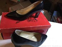 Side view of one black leather heel on red box, showing pointy toe and block heel.