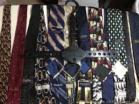 Photo shows 10 designer mens neckties arranged horizontally on a flat surface and hung on a black Hook N Hand hanger labeled with brand name.