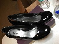 Top-down angled view of both wedge heels showing black patent leather and silver insole with Dexter branding.