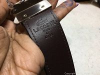 Close-up of Lacoste leather belt stamped with brand, size XL, and made in Spain on brown leather interior side.