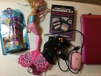 Full lot overview showing Doc McStuffins microphone, mermaid doll, N64 controller, SNES cleaning kit, and pink VTech laptop mouse