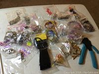 Full lot overview showing multiple plastic bags of beads, charms, findings, colored cords, and a jewelry crimping tool on a brown surface.