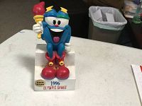 Front view of the 1996 Olympic Games coin bank showing the blue mascot figure holding a torch on a white base.