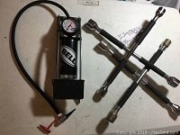 Wide photo showing Bell air pump with gauge and hose next to two 4-way crow bars
