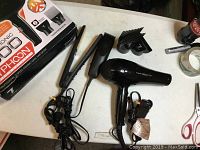 Typhoon 1600W hair dryer, Wall brand clipper set with power cords and attachments, and ceramic flat iron in original box on table.
