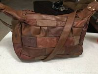 Front and side views of brown leather patchwork shoulder bag with adjustable strap laid on a white table.
