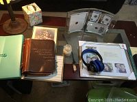 Photo showing the entire collection of items on a glass table including the leather Bible cover, sound disks, headphones, candle, folder, and picture frames.