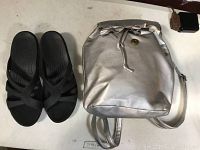 Black Crocs comfort sandals with multiple strap design next to a silver mini backpack laying on a white surface.