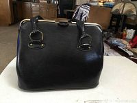 Front view of black leather handbag showing shape, handles, and clasp.