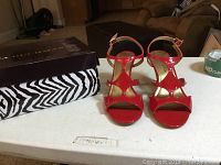 Photo showing the red patent leather high-heel sandals on a white table next to their box and zebra print bag.