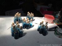Photo showing 25 new clear mini glass bottles filled with blue liquid, cork stoppers, and twine loops, arranged on a table.
