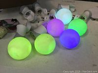 Seven white AirWick scent warmers and six multi-color LED balls illuminated in green, purple, and blue, arranged on a surface.