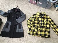 Photo showing both coats laid on carpeted floor: black and grey coat on left, yellow and black plaid coat on right