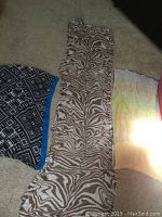 Three scarves laid out on carpet floor: a blue and black geometric patterned scarf folded on the left, a long beige and white animal print scarf in the center, and a pastel tie-dye scarf partially visible on the right.