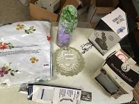 Photo showing queen size linens in floral packaging, clear crystal bowl, glass vase with greenery, boxed LED fountain and scented oil warmer, and towel racks.