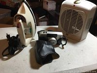 Shows all three items: Canon Z135 camera, leather case, Black & Decker iron, and RE Room Essentials heater fan on a white surface.