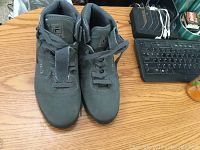 Top down view of pair of grey Fila sneakers with black stripe detailing, laced and placed side by side on a wooden surface near keyboard and other objects.