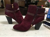 Pair of burgundy suede ankle boots with brown leather straps and gold zipper closure, shown angled side front.