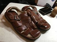 Pair of brown leather Robert David men's sandals, showing front and top side view on a table surface with other items in the background.