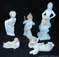 Five porcelain figurines including angels, a boy sweeping, a girl, and a woman with fish displayed on black background.